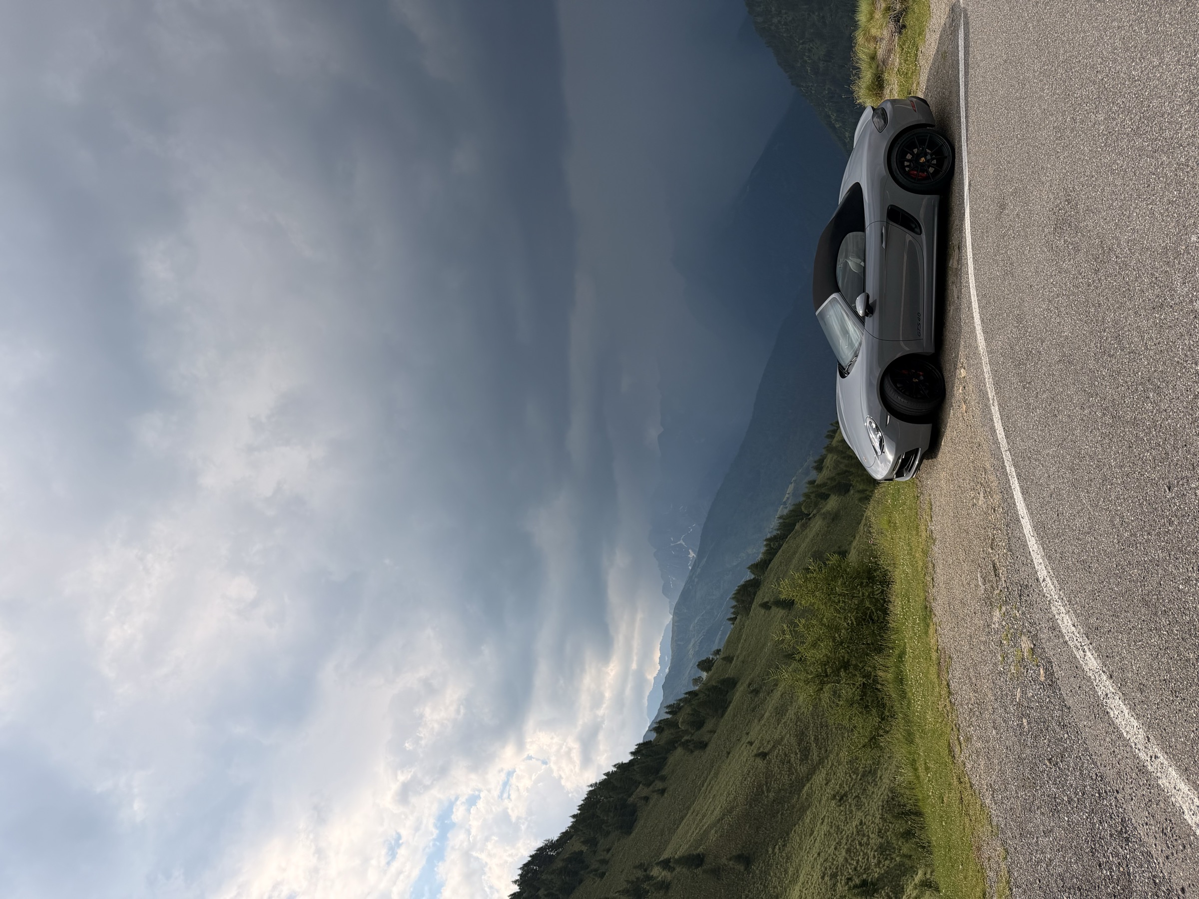 Porsche 718 Boxster GTS 4.0 parked alone on an alpine pass beneath a dark storm sky